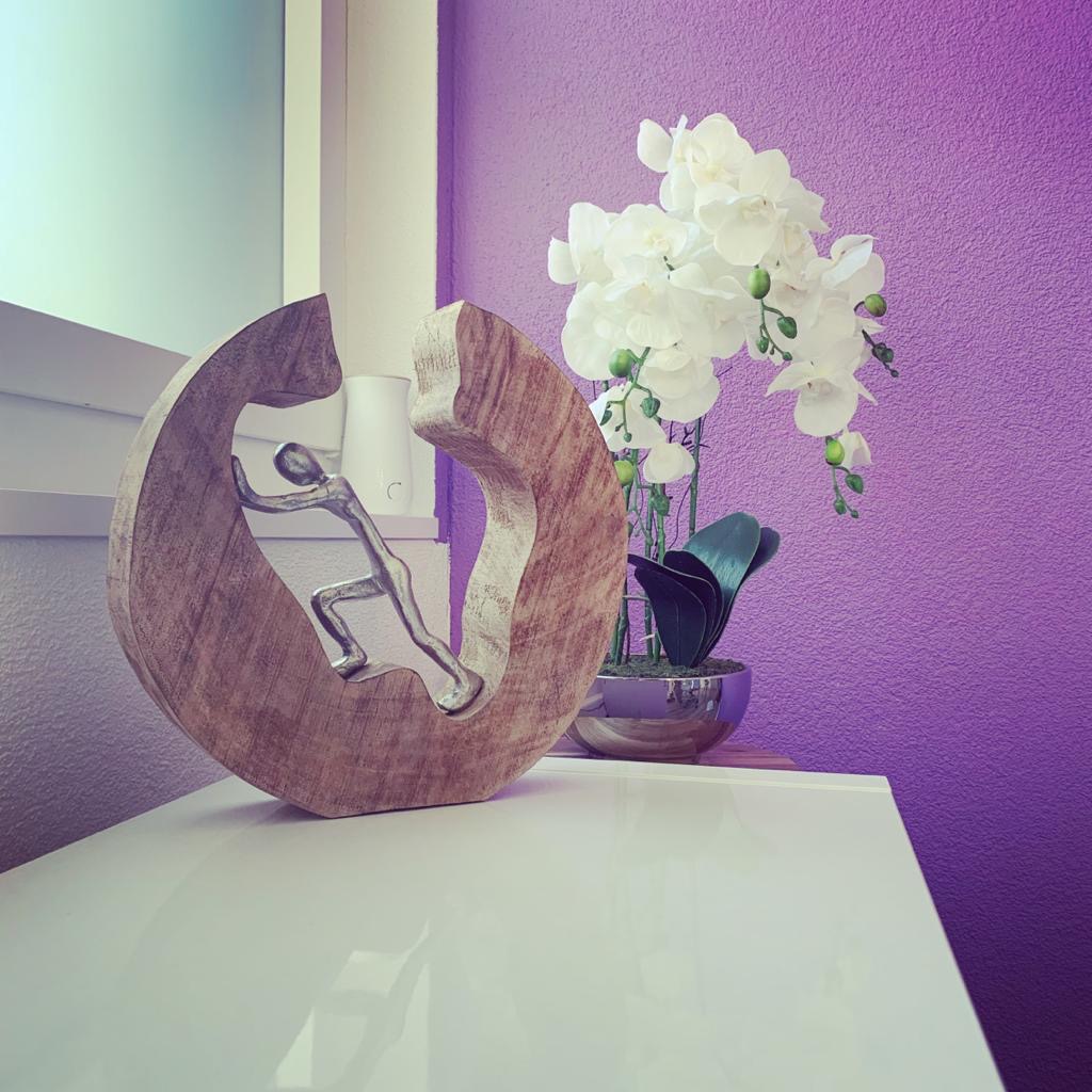 Detailaufnahme aus dem Beratungsbüro: Holzskulptur und Orchidee vor magentafarbener Wand.