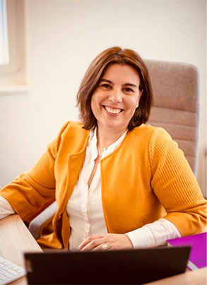 Portrait von Luisa Garrido, Geschäftsinhaberin Prime Consulting GmbH, in orangem Cardigan am Schreibtisch.